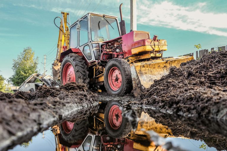 A powerful bulldozer at a construction site, reflecting in a puddle under clear sky.